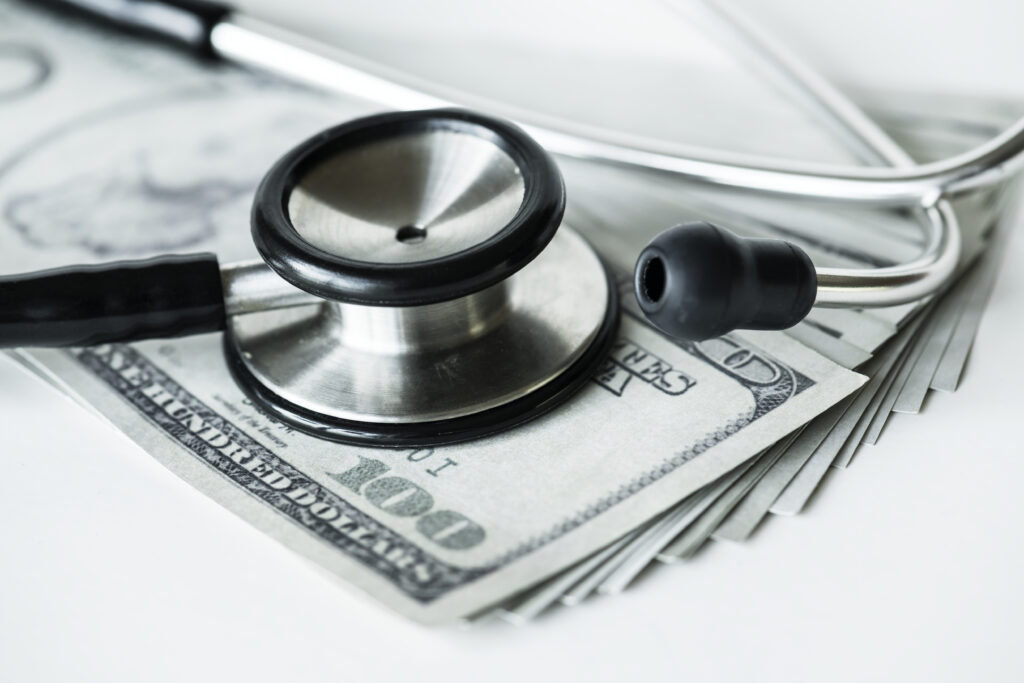 Stethoscope placed on U.S. dollar bills symbolizing the connection between healthcare costs and insurance coverage.