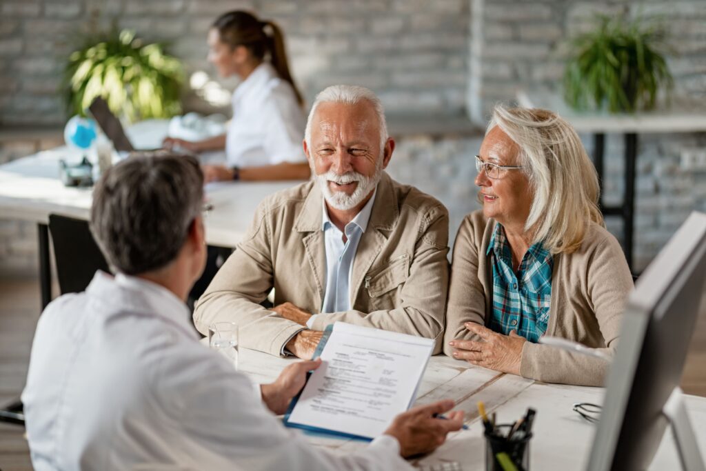 Senior couple discussing health insurance paperwork with a healthcare professional at a desk.