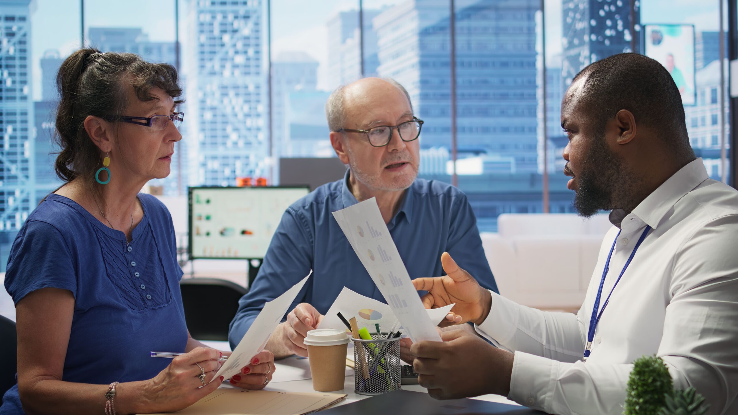 Two older adults reviewing financial documents with a professional advisor while discussing ACA compliant health insurance plans in a modern office setting.