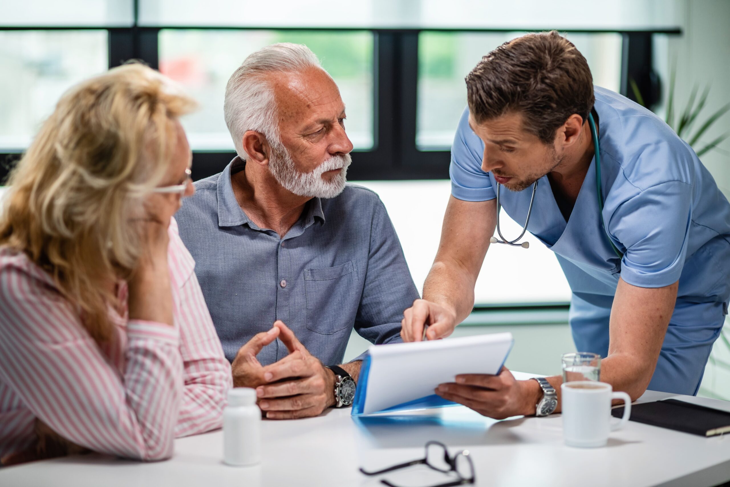Doctor explaining ACA health insurance documents and coverage options to a couple during a medical consultation.